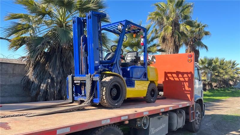 Grúa horquilla azul y amarilla sobre el camión plataforma
